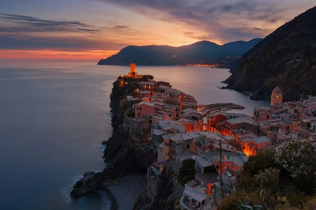 Vernazza em Cinque Terre, Itália, ao pôr do sol com casas coloridas no penhasco e mar calmo ao fundo.